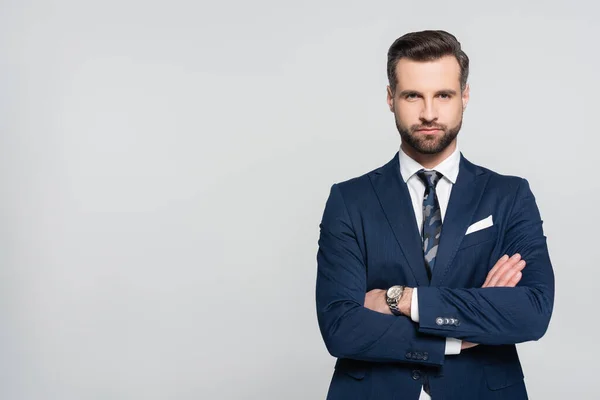 Hombre de negocios barbudo en blazer azul de pie con brazos cruzados aislados en gris - foto de stock