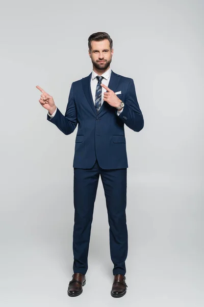 Vista completa del economista en traje azul señalando con los dedos en gris - foto de stock