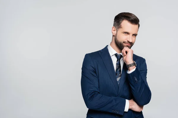 Positive businessman with hand near face looking at camera isolated on grey — стоковое фото