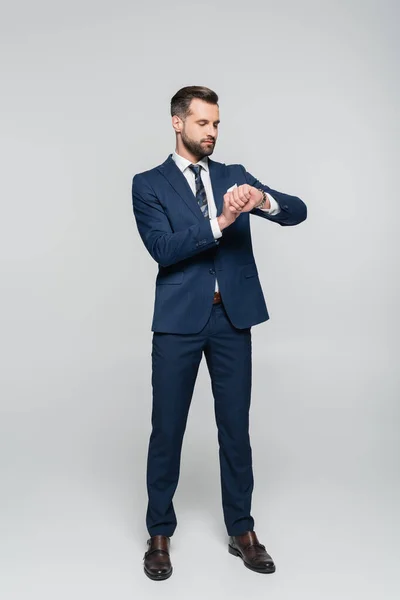 Vue pleine longueur de l'homme d'affaires en costume bleu temps de contrôle sur gris — Photo de stock