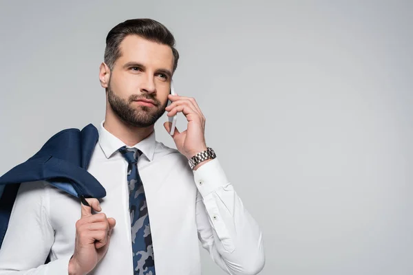 Empresário morena segurando blazer, falando no smartphone e olhando para longe isolado no cinza — Fotografia de Stock