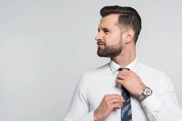 Brunette economist in white shirt adjusting tie while looking away isolated on grey — стоковое фото