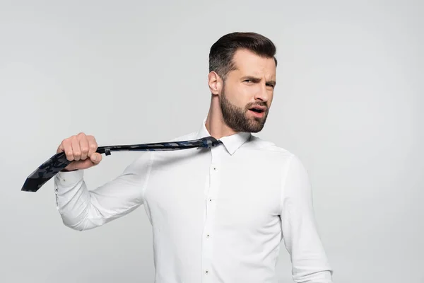 Displeased businessman pulling tie and looking at camera isolated on grey — Stock Photo