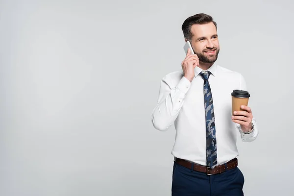 Economista con bebida para llevar sonriendo mientras habla en teléfono inteligente aislado en gris - foto de stock