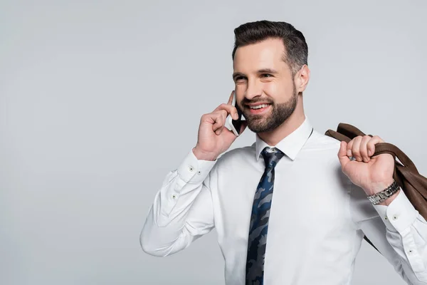 Alegre hombre de negocios en camisa blanca llamando a un teléfono inteligente y mirando hacia otro lado aislado en gris - foto de stock