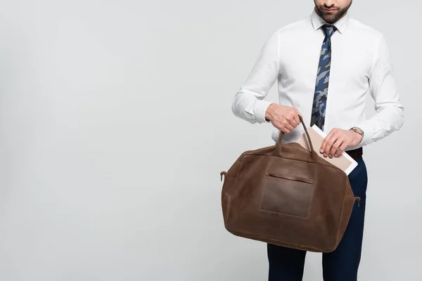 Cropped view of economist putting folder into leather briefcase isolated on grey — Stock Photo