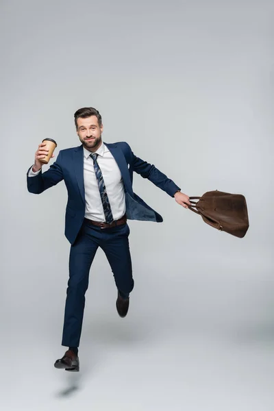 Full length of cheerful economist with coffee to go and leather bag running on grey — Stock Photo