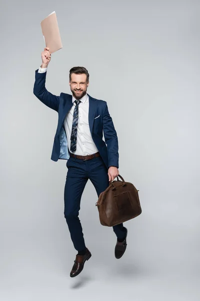 Vista completa del economista excitado con maletín y carpeta levitando sobre gris - foto de stock