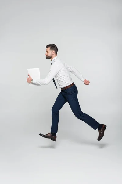 Side view of businessman in white shirt running with digital tablet on grey — Stock Photo