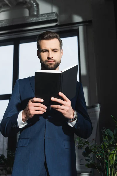 Niedrigwinkel-Ansicht des Geschäftsmannes, der Notizbuch im Büro liest — Stockfoto