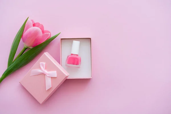Top view of nail polish inside of gift box near tulip on pink — Stock Photo