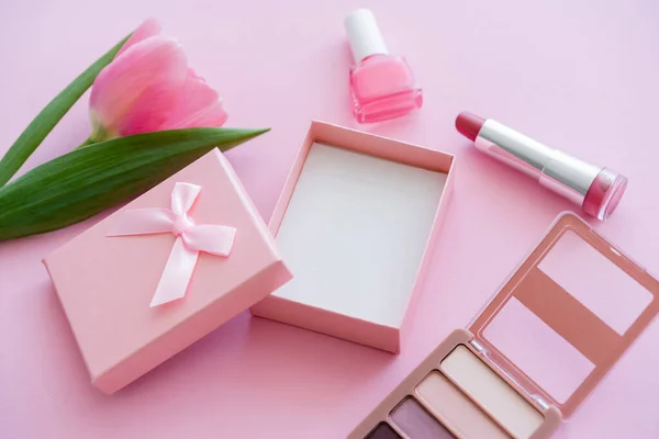 Цветущий тюльпан рядом с декоративной косметикой и подарочной коробкой на розовом — стоковое фото