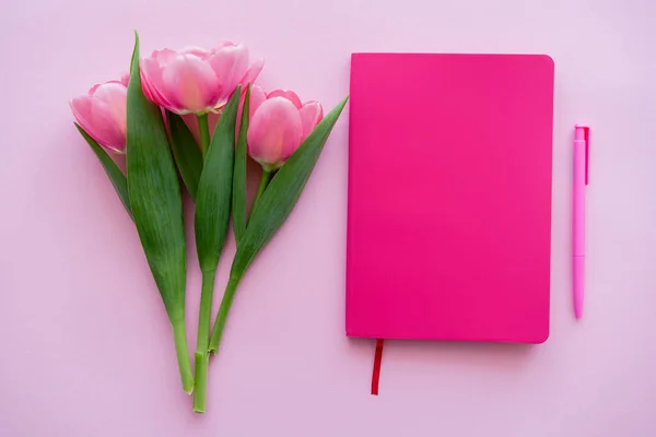 Верхний вид тюльпанов рядом с ноутбуком и ручкой на розовый — стоковое фото