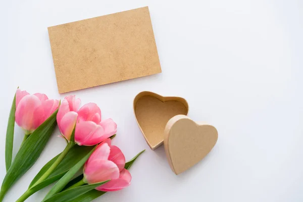 Ansicht von rosa Tulpen in der Nähe von Bastelpapier und herzförmiger Geschenkschachtel auf weiß — Stockfoto