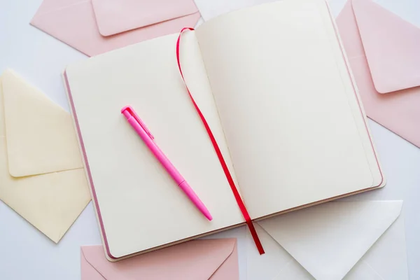 Vue du haut du carnet vierge et du stylo sur les enveloppes pastel sur blanc — Photo de stock