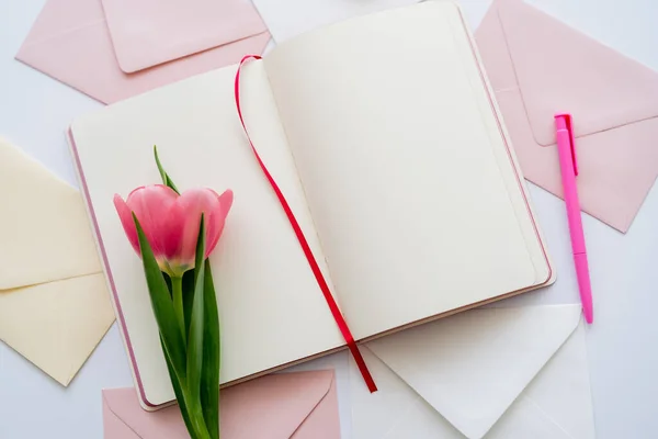 Draufsicht auf rosa Tulpe auf leerem Notizbuch in der Nähe von Umschlägen auf weiß — Stockfoto