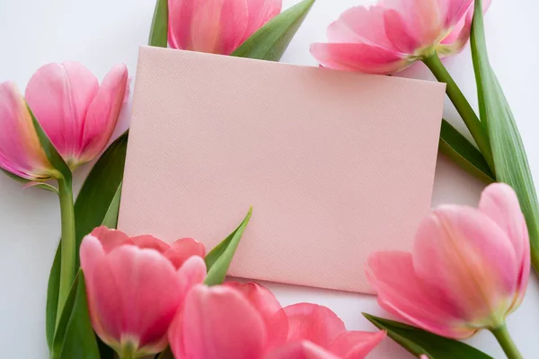 Primer plano de tulipanes rosados cerca de sobre pastel en blanco - foto de stock