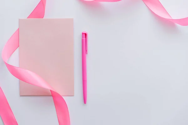 Draufsicht auf Briefumschlag in der Nähe von Stift und rosa Schleife auf weißem Papier — Stockfoto