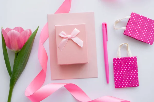 Vue du dessus de la boîte cadeau sur enveloppe près de la tulipe rose et sacs à provisions sur blanc — Photo de stock