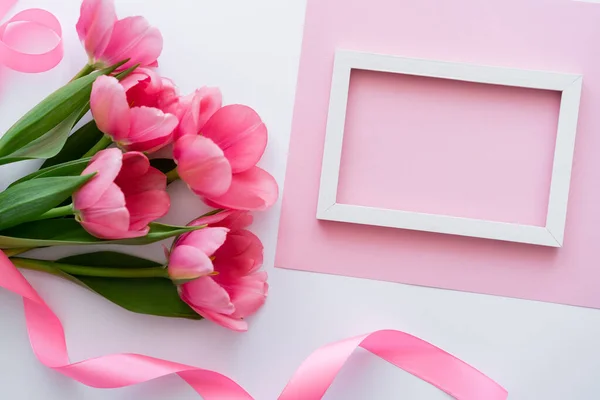 Вид сверху на букет с тюльпанами рядом с лентой и рамкой на белом и розовом — стоковое фото
