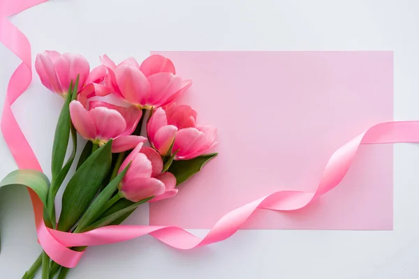 Vista dall'alto di bouquet con tulipani vicino al nastro e carta rosa su bianco — Foto stock