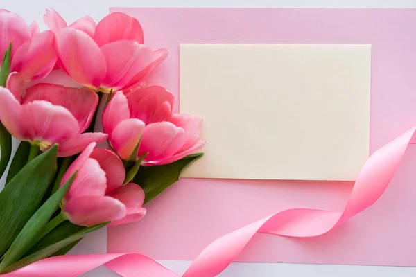 Vista dall'alto di mazzo con tulipani vicino a nastro e busta gialla su bianco e rosa — Foto stock