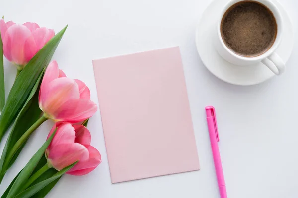 Vue du dessus de tasse de café près de tulipes roses, papier et stylo sur blanc — Photo de stock