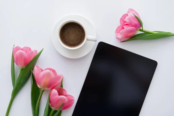 Vista superior da xícara de café perto de tulipas rosa e tablet digital com tela em branco no branco — Fotografia de Stock