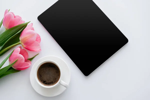 Вид зверху чашки кави біля тюльпанів і цифрового планшета з порожнім екраном на білому — стокове фото