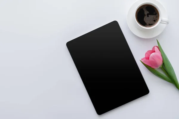 Vista superior da xícara de café perto de tulipa rosa e tablet digital com tela em branco no branco — Fotografia de Stock
