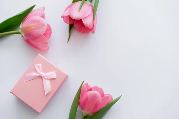 Vista superior da caixa de presente perto de flores rosa brilhantes no branco — Fotografia de Stock