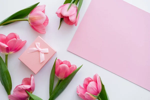 Top view of gift box near bright pink flowers and blank paper on white — Stock Photo