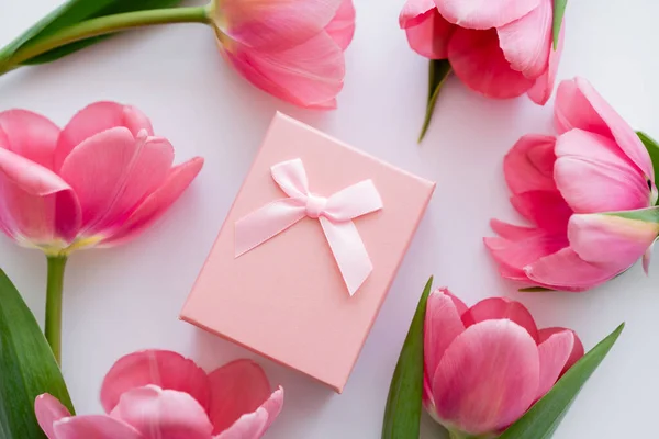 Вид подарочной коробки рядом с ярко-розовыми цветами на белом — стоковое фото