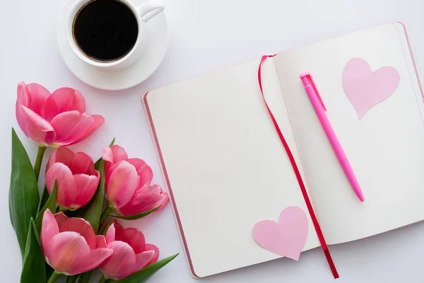 Vista superior de los tulipanes cerca del cuaderno con corazones de papel y taza de café en blanco - foto de stock
