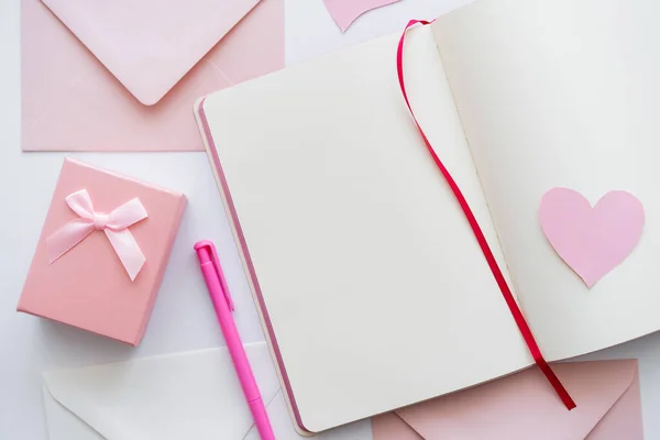 Top view of notebook with paper heart near envelopes and gift box on white — Stock Photo