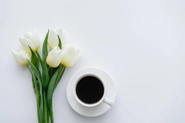 Draufsicht auf Tulpen in der Nähe von Tasse mit Kaffee auf Untertasse auf Weiß — Stockfoto