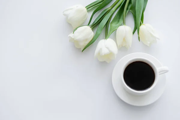 Vista superior da xícara com café no pires perto de tulipas em branco — Fotografia de Stock