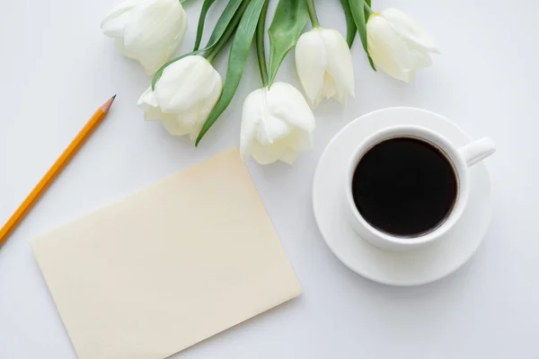 Vue du dessus de l'enveloppe avec crayon près de la tasse avec café et tulipes sur blanc — Photo de stock