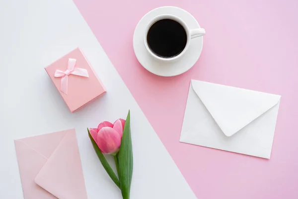 Vista superior de envelopes perto de xícara com café, caixa de presente e tulipa em branco e rosa — Fotografia de Stock