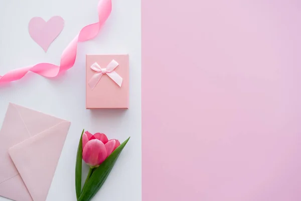 Vue de dessus de l'enveloppe proche du présent avec arc et tulipe sur blanc et rose — Photo de stock