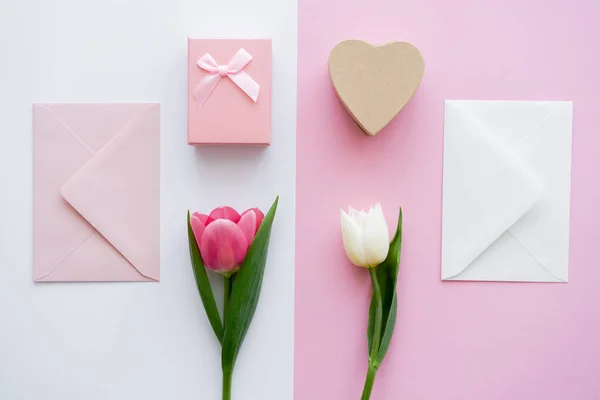 Vista dall'alto di buste vicino a scatole regalo e tulipani su bianco e rosa — Stock Photo