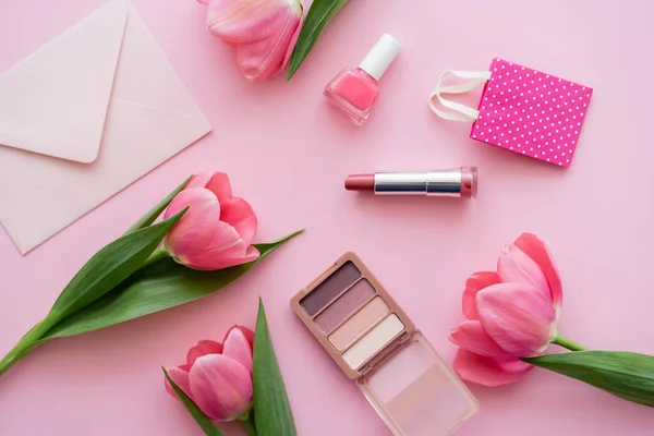 Top view of blooming tulips near decorative cosmetics and envelope on pink — Stock Photo