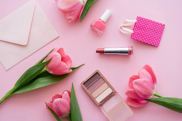 Vista dall'alto di tulipani fioriti vicino a cosmetici decorativi e busta su rosa — Foto stock