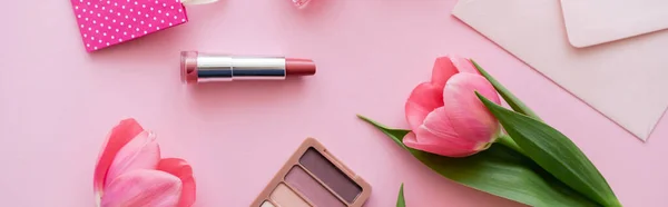 Вид на цветущие тюльпаны рядом с декоративной косметикой и конвертом на розовом, баннер — стоковое фото