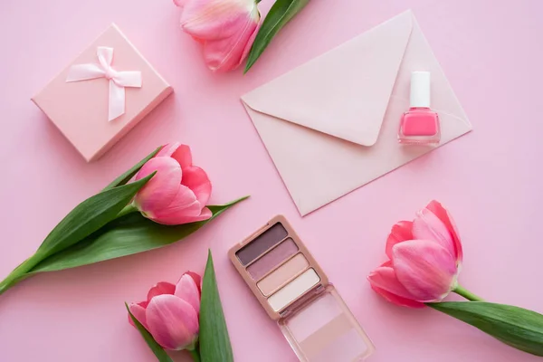 Top view of blooming tulips near decorative cosmetics, present and envelope on pink — Stock Photo