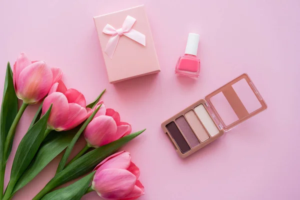 Top view of blooming tulips near decorative cosmetics and gift box on pink — Stock Photo