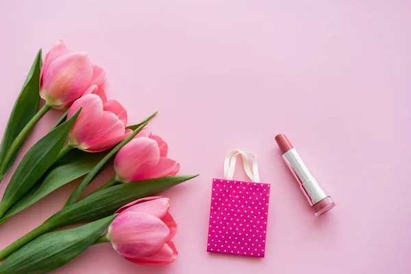Вид зверху квітучих тюльпанів біля помади та маленький торговельний мішок на рожевому — стокове фото