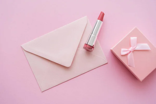 Vista superior de lápiz labial cerca de sobre y caja de regalo en rosa - foto de stock