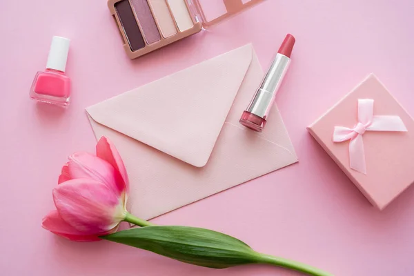 Vue de dessus de la tulipe en fleurs près des cosmétiques décoratifs, enveloppe et boîte cadeau sur rose — Photo de stock