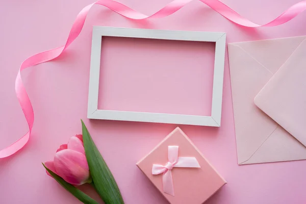 Верхний вид тюльпан рядом рамка, конверт и подарочная коробка на розовый — стоковое фото